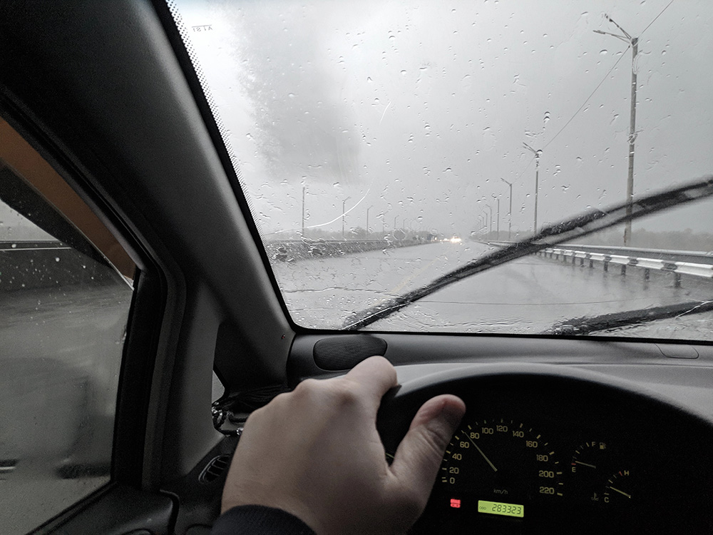 A first person view of a man driving a car in a rainy day