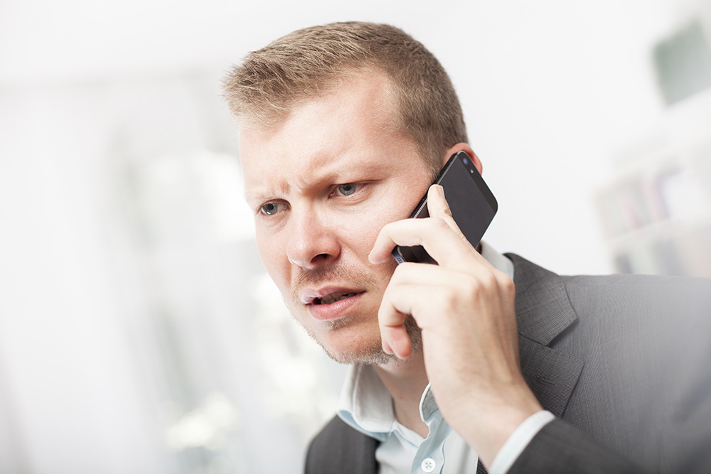Anxious businessman taking a mobile phone call frowning with a worried expression as he listens to the conversation